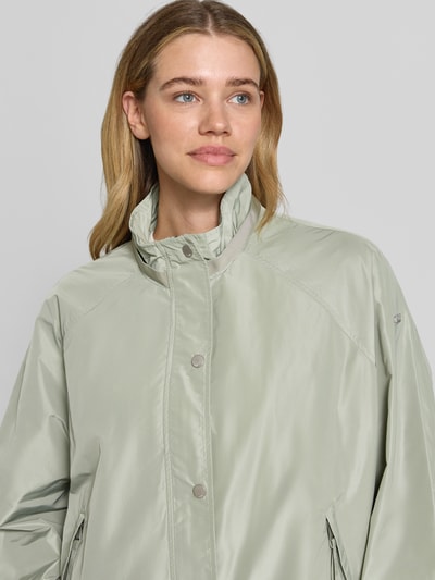 Frauenmodel trägt Jacke mit Kapuze Modell 'CICATA' von CINQUE in hellgrün, glatte Textur, Stehkragen, Nahaufnahme Oberkörper.