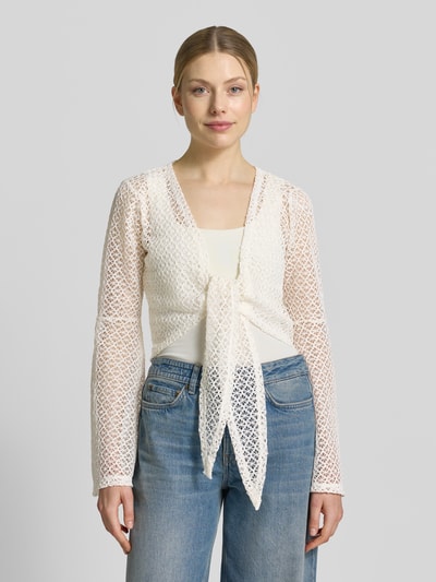 Frauenmodel trägt Strickjacke mit Knotendetail und Trompetenärmeln von Apricot in Weiß, semitransparent, geometrische Struktur, Ganzkörperansicht von vorne. Rückenlänge 43 cm, Ärmellänge 67 cm bei Größe S.