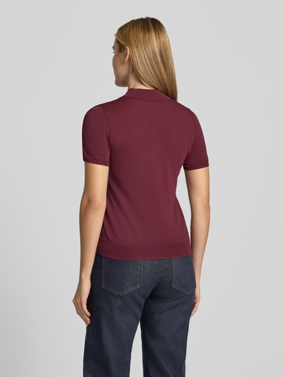 Frauenmodel trägt Poloshirt aus Viskose-Mix Modell 'LUXEN' von MANGO in Dunkelrot, tailliert, gerippte Abschlüsse, Ganzkörperansicht Rückansicht.