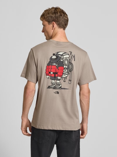Männermodel trägt T-Shirt aus reiner Baumwolle Modell 'Gear Up Get Out' von The North Face in Beige mit Logo-Print, Ganzkörperansicht Rückansicht.