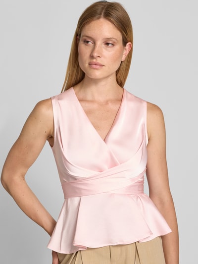 Frauenmodel trägt Blusentop in Wickel-Optik Modell 'Risetta' von Neo Noir in zartem Rosa, glatter Stoff, V-Ausschnitt, Nahaufnahme Oberkörper. Material-Mix mit Stretch-Anteil, Slim Fit, Rückenlänge bei Größe 36: 56 cm.