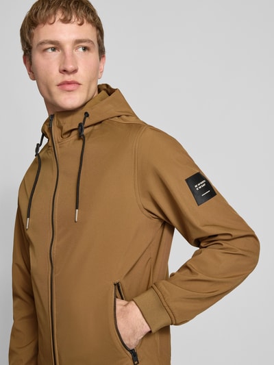 Mannenmodel draagt Softshelljacke mit Reißverschlusstaschen van Jack & Jones in regular fit, bruin, capuchon, rits, zakken, nahaufnahme bovenlichaam.