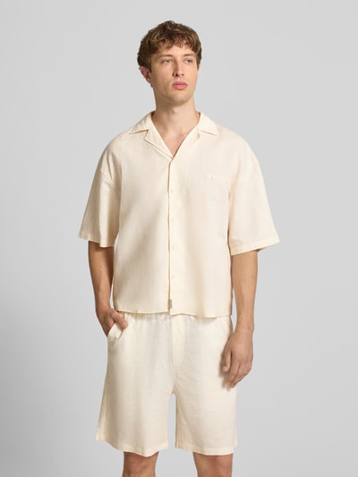 Męski model nosi Relaxed Fit Leinenhemd mit Label-Stitching od ANOTHER COTTON LAB z czystego lnu, kremowy kolor, guzik, krótki rękaw, widok całej sylwetki z przodu