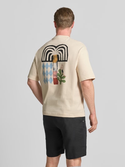 Männermodel trägt Relaxed Fit T-Shirt aus reiner Baumwolle Modell 'NORMAN' von Selected Homme in Beige mit buntem Print, Herren T-Shirt, Ganzkörperansicht Rückansicht.