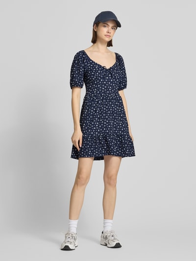 Frauenmodel trägt Minikleid mit Puffärmeln Modell 'HILLARY' von Only in dunkelblau mit weißem floralem Muster, Crêpe-Struktur, Ganzkörperansicht von vorne.