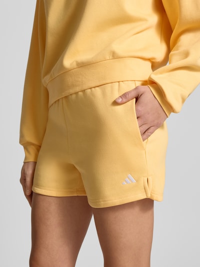 Kobiece modelka nosi Shorts mit Logo und elastischem Bund od adidas Sportswear, kolor żółty, bawełniana mieszanka, regular fit, logo, zbliżenie na biodra.