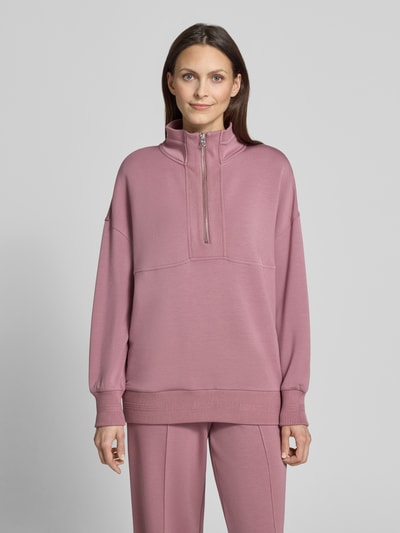 Frauenmodel trägt Damen Sweatshirt mit Troyer-Kragen Modell 'molly' von VARLEY, Viskose-Mix mit Stretch-Anteil, Relaxed-Fit, rosafarbene Oberfläche, kurzer Reißverschluss, überschnittene Schultern, gerippte Ärmelabschlüsse, Ganzkörperansicht von vorne.