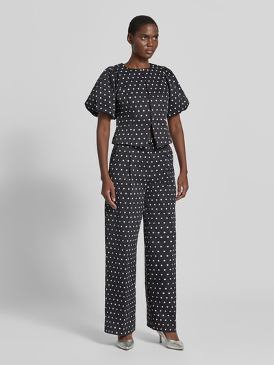 Frauenmodel trägt Slim Fit Bluse im Allover-Look Modell 'ANELA' von Neo Noir mit weißen Punkten, Rundhalsausschnitt, Puffärmel, Hakenverschluss, schwarze Grundfarbe, kombiniert mit weiter Hose, Ganzkörperansicht von vorne.