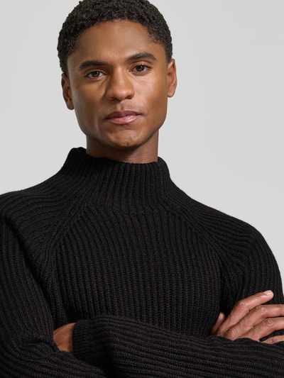 Männermodel trägt Regular Fit Strickpullover mit elastischen Abschlüssen von DRYKORN, schwarzer Material-Mix mit Rollkragen, Nahaufnahme Oberkörper.