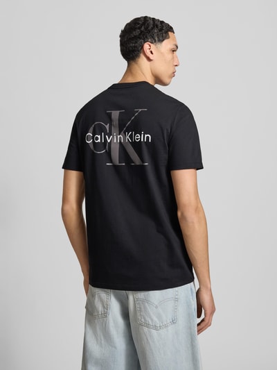Männermodel trägt Regular Fit T-Shirt mit Logo-Print von Calvin Klein Jeans in Schwarz, Reine Baumwolle, Rundhalsausschnitt, Rückenlänge 68 cm, Ganzkörperansicht Rückansicht.
