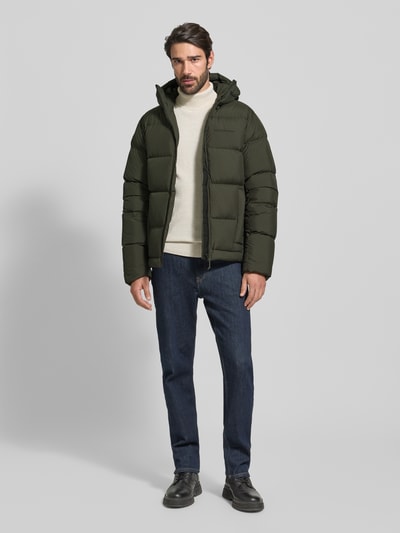 Mannelijk model draagt donkergroene Donsjack met Labelstitching van PEAK PERFORMANCE, donsverenvulling, regular fit, capuchon, ritssluiting, steekzakken, ruglengte 76 cm, schouderbreedte 51 cm, borstwijdte 59 cm, mouwlengte 68 cm. Ganzkörperansicht von voren.