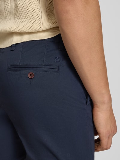 Männermodel trägt Regular Fit Shorts mit Münztasche von Superdry, dunkelblau, mieszanka bawełny, kieszonka na monety, tylna kieszeń, zapięcie na guzik i zamek błyskawiczny, szerokość w rozmiarze 32: 44 cm, długość wewnętrzna nogawki w rozmiarze 32: 20 cm, detailaufnahme z tyłu.