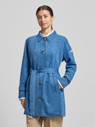 Frauenmodel trägt Trenchcoat mit Bindegürtel Modell 'CORDELIA' von Frieda & Freddies in Blau, Umlegekragen, Knopfleiste, Material-Mix mit Stretch-Anteil, taillierter Schnitt, Label-Detail, Ganzkörperansicht von vorne.
