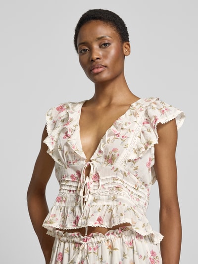 Frauenmodel trägt Blusentop mit V-Ausschnitt und Schnürung von Neo Noir aus reiner Baumwolle, florales Muster, Rüschen, Slim Fit, Nahaufnahme Oberkörper.