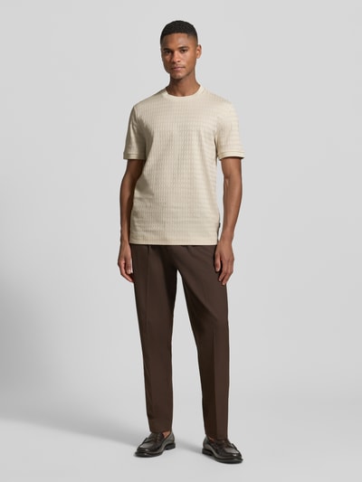 Männermodel trägt Regular Fit T-Shirt aus reiner Baumwolle Modell 'THOMSON' von BOSS in Beige mit feinem Strukturmuster, Ganzkörperansicht von vorne.