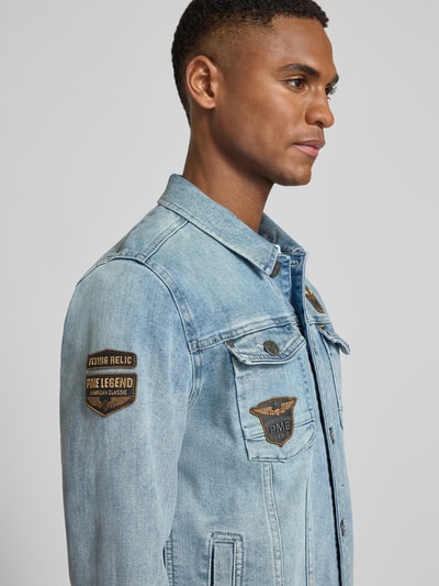 Männermodel trägt Jeansjacke mit Label-Patches und Brusttaschen von PME Legend, niebieski denim, bawełniany miks, krótki kołnierz, prosty krój, naszywki, widoczne kieszenie, detal na guzik, perspektywa z przodu, zbliżenie na górną część ciała
