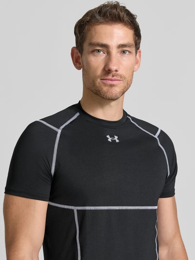 Männermodel trägt T-Shirt mit Logo-Print und Raglanärmel van Under Armour, Materiaalmix met stretch, elite fit, ronde hals, zwart, logoprint, raglanmouwen, ruglengte maat M 69 cm, Nahaufnahme Oberkörper