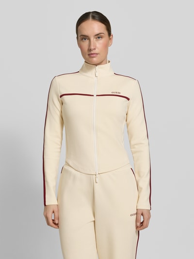 Frauenmodel trägt Slim Fit Sweatjacke mit Stehkragen Modell 'Jasmine' von Guess Activewear in Creme mit roten Akzenten, Nahaufnahme Oberkörper.