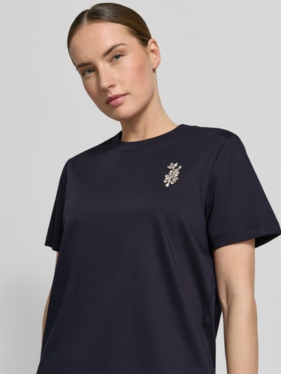 Frauenmodel trägt T-Shirt mit Ziersteinbesatz von Comma in Dunkelblau aus reiner Baumwolle, Regular-Fit, Rundhalsausschnitt, Nahaufnahme Oberkörper. Rückenlänge bei Größe 36: 58 cm.