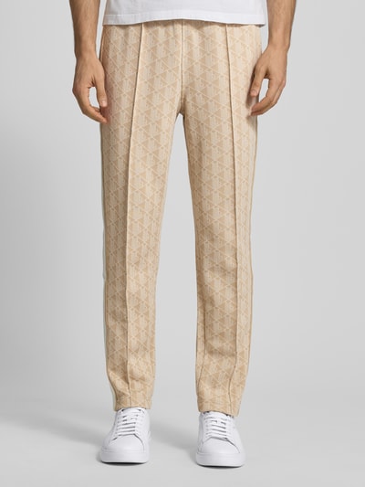 Mężczyznamodel nosi Regular Fit Sweathose mit Baumwoll-Anteil od Lacoste, efekt: wzór na całej powierzchni, krój regular fit, naszywka z logo, paski w kontrastowym kolorze, wpuszczane kieszenie, wykończenie: dzianina dresowa, kolor beżowy, widok na całe nogi z przodu.