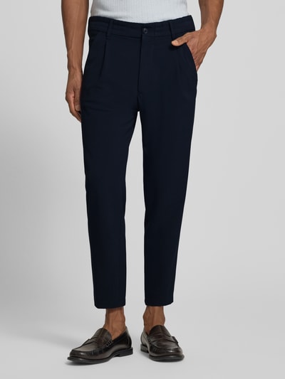 Męski model nosi Hose mit Eingrifftaschen Modell 'CHASY' od Drykorn w kolorze granatowym, krój tapered fit, mieszanka materiałów z dodatkiem wiskozy, elastyczny pas, kieszenie francuskie, szerokość w rozmiarze 32/32: 42 cm, długość nogawki od wewnątrz: 66 cm, zdjęcie całej sylwetki z przodu.