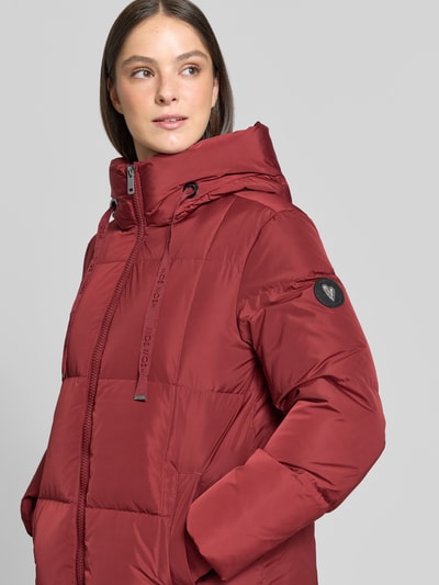 Frauenmodel trägt Regular Fit Mantel in Stepp-Optik Modell 'Nova' von MOS MOSH in Rot, Zweiwege-Reißverschluss, Kapuze, Nahaufnahme Oberkörper. Rückenlänge 102 cm, Schulterbreite 42 cm, Brustweite 46 cm, Ärmellänge 64 cm.