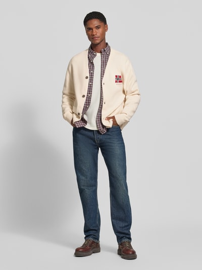Männermodel trägt Cardigan mit Logo-Stitching Modell 'TARANGER' von Napapijri, cremefarben, Regular Fit, V-Ausschnitt, Eingrifftaschen, Ganzkörperansicht von vorne.