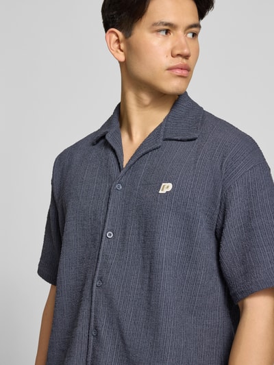 Mannenmodel draagt Regular fit vrijetijds overhemd met label-patch model 'LIBCO' van Pegador, katoenmix, reverskraag, korte mouwen, knoopsluiting, donkergrijs met structuur, detailopname bovenlichaam.