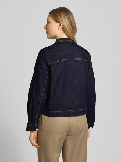 Modelka nosi Regular Fit Jeansjacke aus Baumwoll-Mix von Tom Tailor, ciemny denim, wyhaftowany motyw, splot twill, mieszanka bawełny, fason/krój: krój regular fit, wykładany kołnierz, listwa z zatrzaskami, pas na plecach, kieszenie na piersi, długi rękaw z mankietami. Ganzkörperansicht Rückansicht.