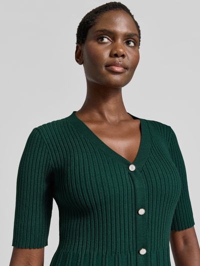 Frauenmodel trägt Strickkleid in Minilänge mit Viskose-Anteil von Christian Berg Woman in Dunkelgrün, Ripp-Optik, Nahaufnahme Oberkörper.