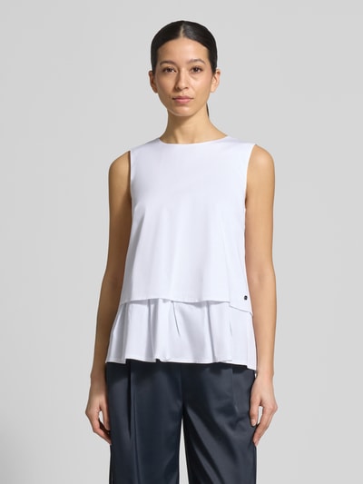 Modelka nosi Blusenshirt mit Volantsaum und Rundhalsausschnitt von Marc Cain z mieszanki bawełny i wiskozy, prosty krój, okrągły dekolt, dół obszyty falbaną, zamek błyskawiczny z tyłu, długość tyłu w rozmiarze 36: 59 cm, widok całej sylwetki z przodu.