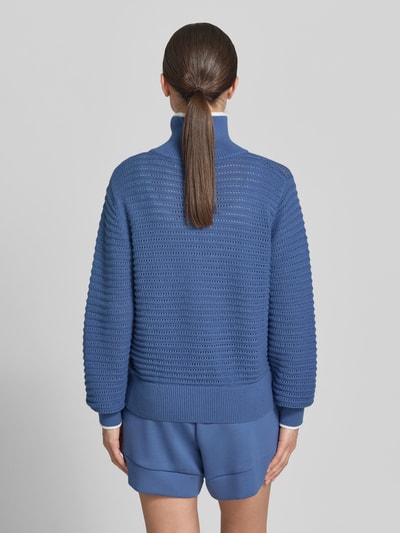 Frauenmodel trägt Strickpullover mit Reißverschluss Modell 'morwenna' von VARLEY aus Reine Baumwolle, Regular-Fit, Rückenlänge 61 cm, Ärmellänge 76 cm, Strukturstrick in Blautönen, Ganzkörperansicht Rückansicht.