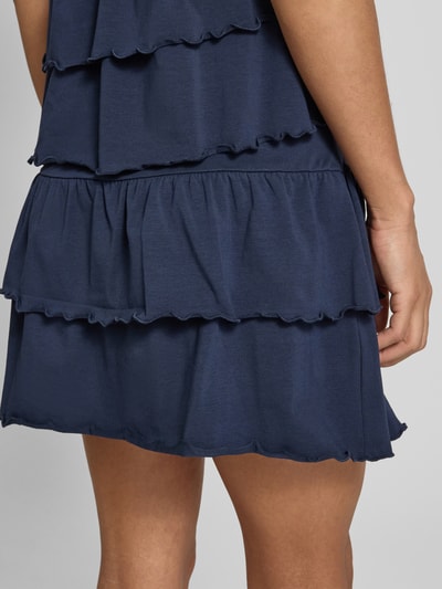 Frauenmodel trägt Minirock im Stufen-Look von REVIEW aus dunkelblauem Baumwoll-Elasthan-Mix mit Volants, Nahaufnahme Oberschenkel.