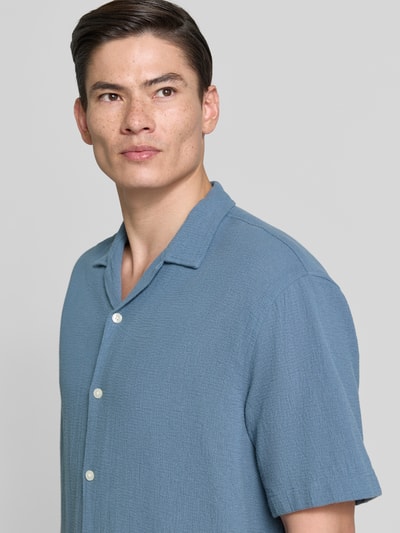 Männermodel trägt Relaxed Fit Freizeithemd aus reiner Baumwolle Modell 'RLXCAL' von SELECTED HOMME in Blau mit Bowling-Kragen, Nahaufnahme Oberkörper.