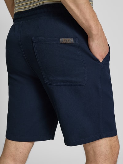 Męski model nosi Shorts mit Strukturmuster Modell 'JAIDEN' od Jack & Jones, czysta bawełna, krój regular fit, ciemnoniebieski, elastyczny pas, tunel, szerokość w rozmiarze M: 43 cm, długość wewnętrzna nogawki: 23 cm, tekstura widoczna, widok z tyłu całej sylwetki.