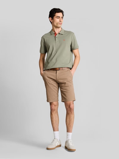 Męski model nosi Regular Fit Poloshirt aus reiner Baumwolle von Tom Tailor, kolor jednolity, logo z przodu, krój regular fit, bawełna pikowana, przód z krótkim rękawem, kołnierz polo, zapięcie na dwa guziki, rozcięcia po bokach, widok całej sylwetki z przodu