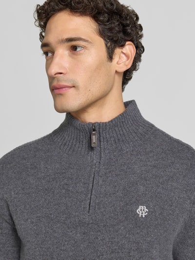 Männermodel trägt Regular Fit Strickpullover aus reiner Wolle von MCNEAL in Grau mit Logo-Stickerei und Troyer-Kragen, Nahaufnahme Oberkörper.