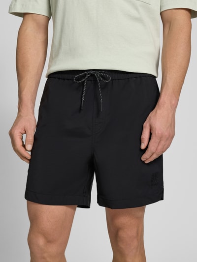 Männermodel trägt Regular Fit Shorts mit Label-Applikation Modell 'COLAS262S' von HUGO, Optik: Unifarben, Kontraststreifen, Eingrifftaschen, Bundabschluss elastisch mit Tunnelzug, Nahaufnahme Oberkörper.
