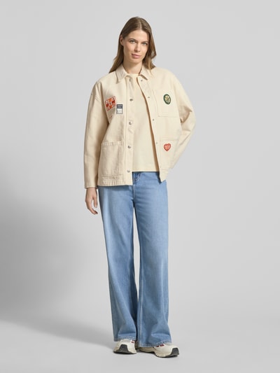 Frauenmodel trägt Regular Fit Hemdjacke mit Motiv-Patches von Jake*s Casual in Beige mit aufgesetzten Taschen, Umlegekragen, Reine Baumwolle, durchgängige Knopfleiste, kombiniert mit weiter Jeans, Ganzkörperansicht von vorne.