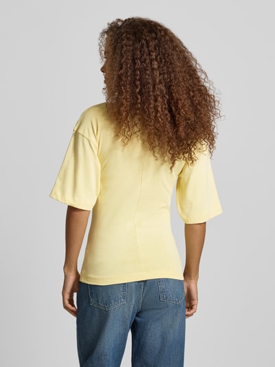 Kobiece model prezentuje damski t-shirt z bawełny, prosty krój, model 'MALLE' od Topshop, żółty, okrągły dekolt, długość tyłu 66 cm w rozmiarze S, marszczenia z wiązaniem, obniżone ramiona, widok całej sylwetki z tyłu