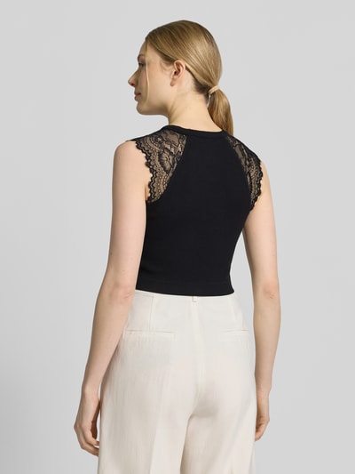 Modelka kobieca ma na sobie Crop Top mit Spitzenbesatz Modell 'MILLIE' od Guess z mieszanki materiałów ze stretchem, czarny, krój slim fit, koronkowe detale, zdjęcie całej sylwetki z tyłu.