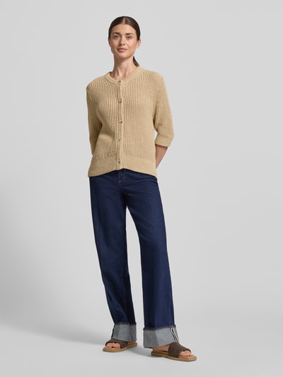 Modelka nosi Strickshirt mit 1/2-Arm Modell 'Donousa' od OPUS, krój regular fit, okrągły dekolt, listwa guzikowa, długość tyłu 60 cm, długość rękawów 36 cm; beżowa dzianina, proste jeansy, piaskowa faktura, widok całej sylwetki z przodu.