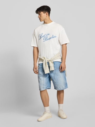 Männermodel trägt T-Shirt mit Logo- und Statement-Stitching von REVIEW aus Reine Baumwolle, Gerader-Schnitt, helle Farben, Ganzkörperansicht von vorne. Rückenlänge Größe M: 64 cm.
