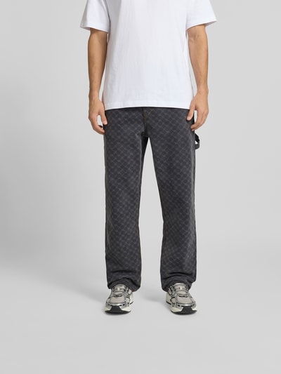 Männermodel trägt Wide Fit Jeans mit Allover-Print von DAILY PAPER, schwarze Baumwolle, 5-Pocket, Ganzkörperansicht von vorne.