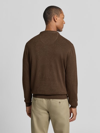 Męski model nosi sweter z dzianiny z bawełny z wyhaftowanym logo Strickpullover aus reiner Baumwolle mit Logo-Stickerei von Fynch-Hatton, imitacja dzianiny, krój regular fit, długi rękaw, opadające ramiona, okrągły dekolt, prążkowane wykończenia, długość tyłu w rozmiarze M: 68 cm, długość rękawa w rozmiarze M: 69 cm, widok całej sylwetki z tyłu.