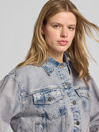 Frauenmodel trägt Oversized Jeansjacke mit Brusttaschen und Label-Patch von Guess Jeans aus hellblauem Baumwoll-Mix mit Stretch-Anteil, Nahaufnahme Oberkörper.