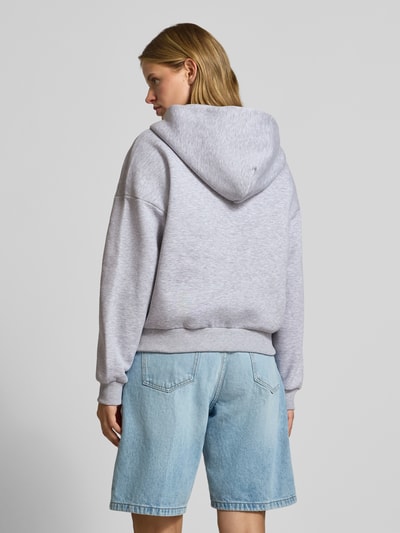 Frauenmodel trägt Sweatjacke mit Logo und Känguru-Tasche von REVIEW, hellgrauer Baumwoll-Mix, Relaxed Fit, Ganzkörperansicht Rückansicht.