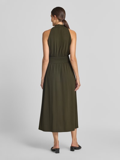 Frauenmodel trägt Midikleid aus Viskose-Mix von Samsøe Samsøe in Olivgrün mit Smok-Detail, taillierte Passform, Ganzkörperansicht Rückansicht.