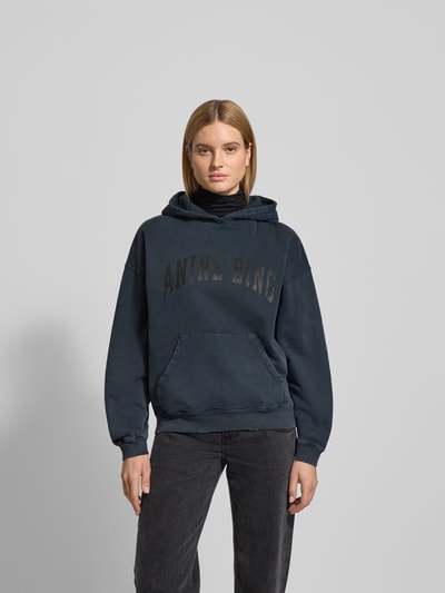 Frauenmodel trägt Oversized Hoodie mit Logo-Stitching von Anine Bing in Dunkelblau, Reine Baumwolle, Oversized-Fit, Känguru-Tasche, elastische Abschlüsse, Rückenlänge bei Größe S 63 cm, Ganzkörperansicht von vorne.