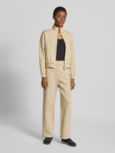 Frauenmodel trägt Sweatjacke mit Reißverschluss von Armani Exchange im Allover-Label-Print, lockere Passform, Beige, Ganzkörperansicht von vorne.